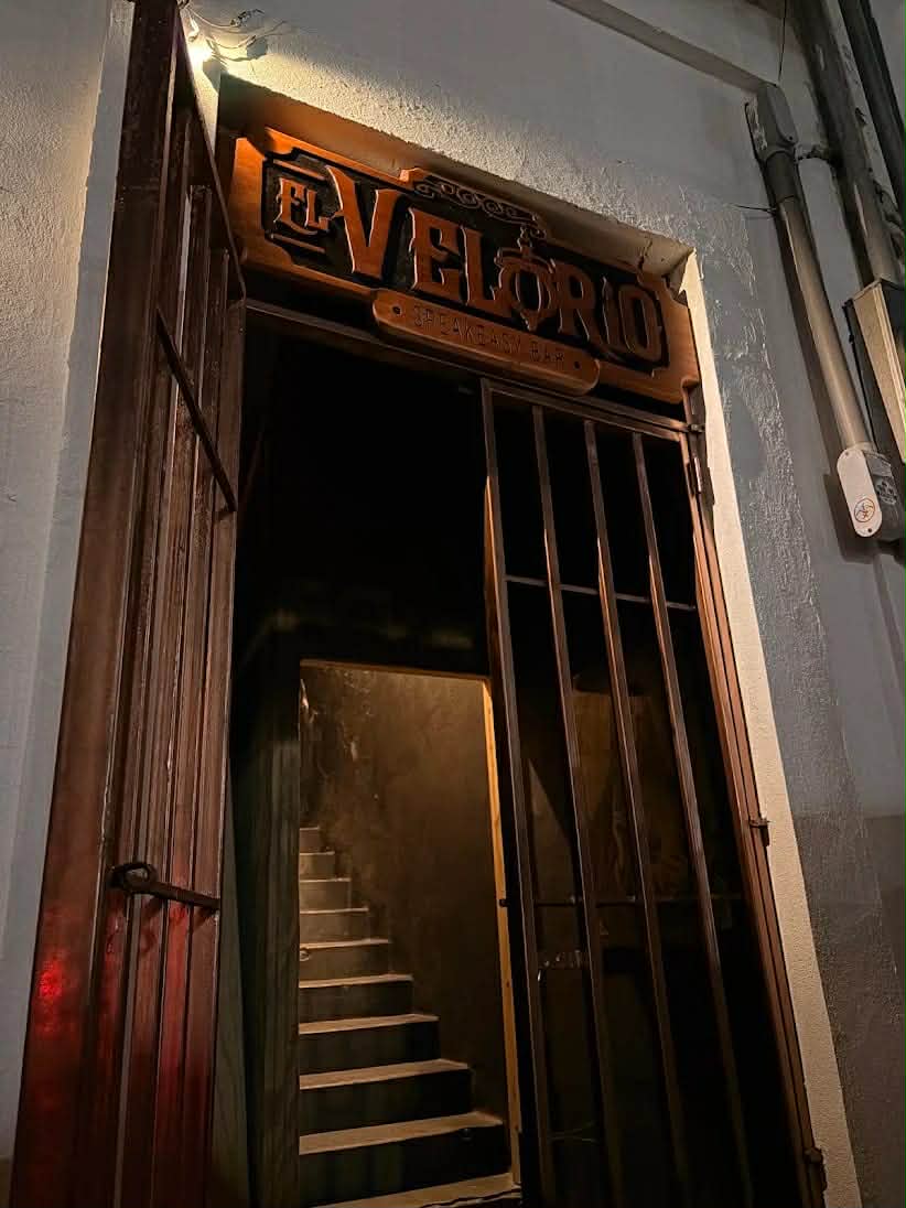 Entrada de El Velorio con letrero de madera y escalera al segundo piso
